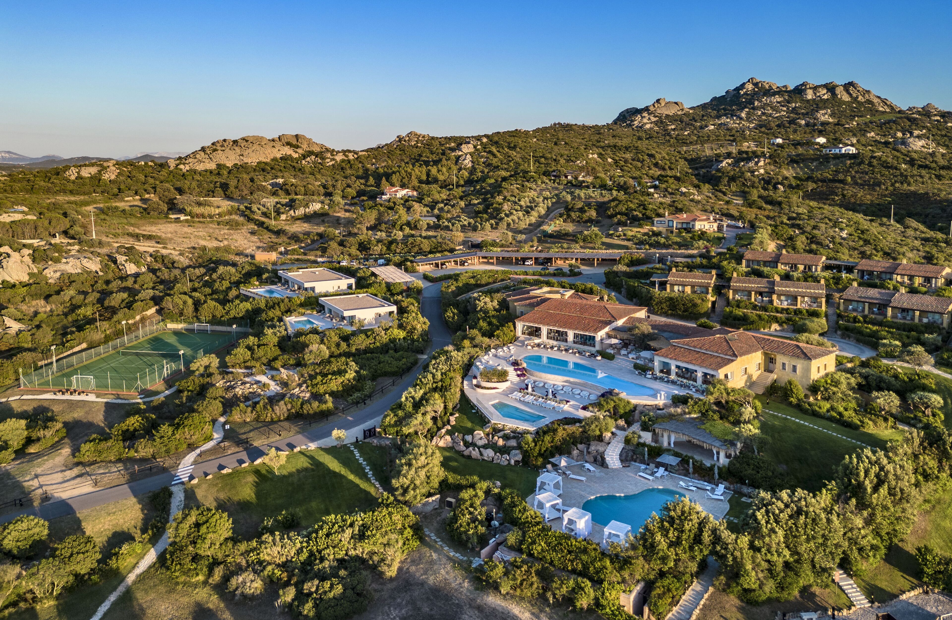 Vista aérea de un complejo turístico con varias villas, una piscina y una cancha de tenis.