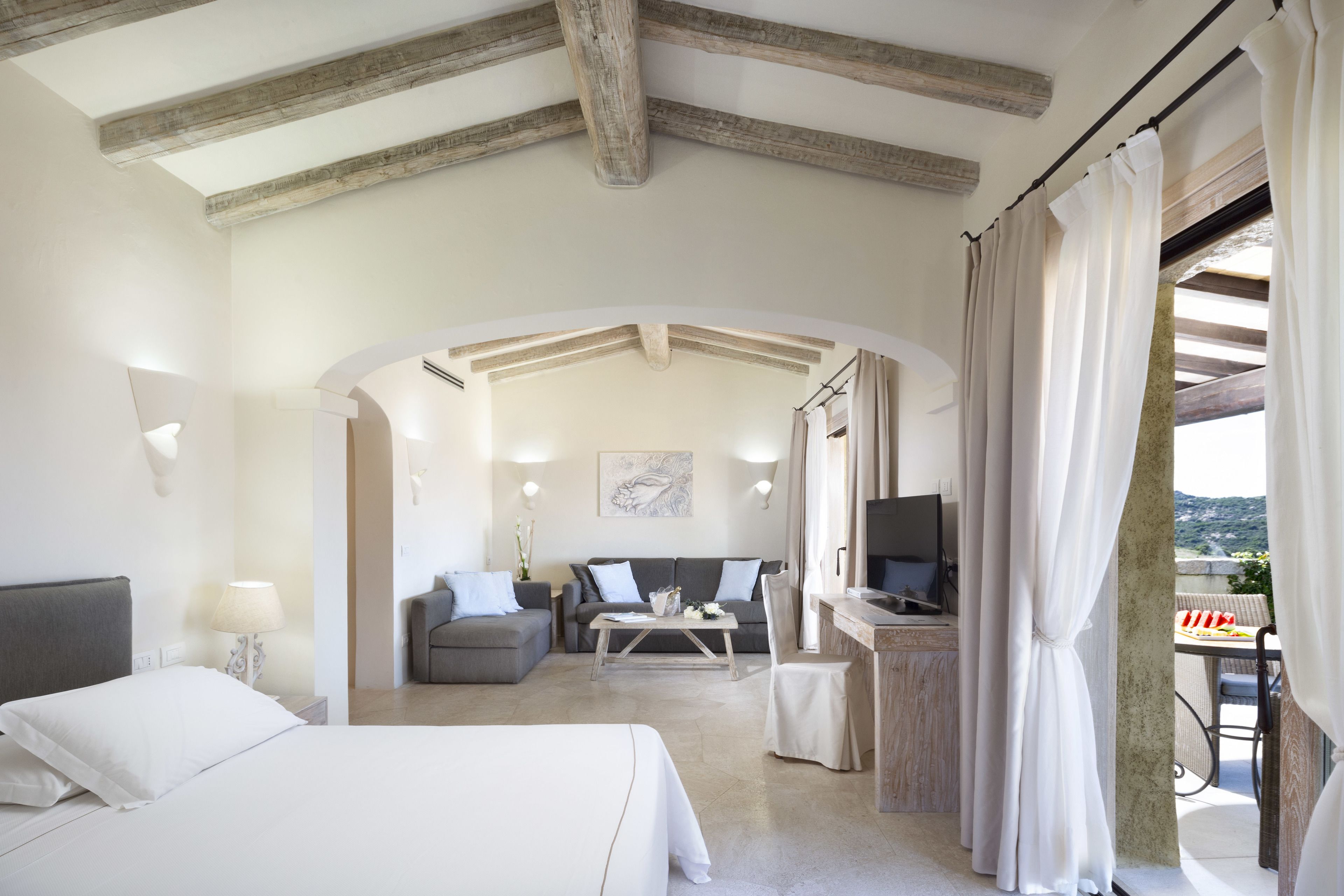 A hotel room with a bed, a sofa, a desk with a computer, and a balcony with a view.
