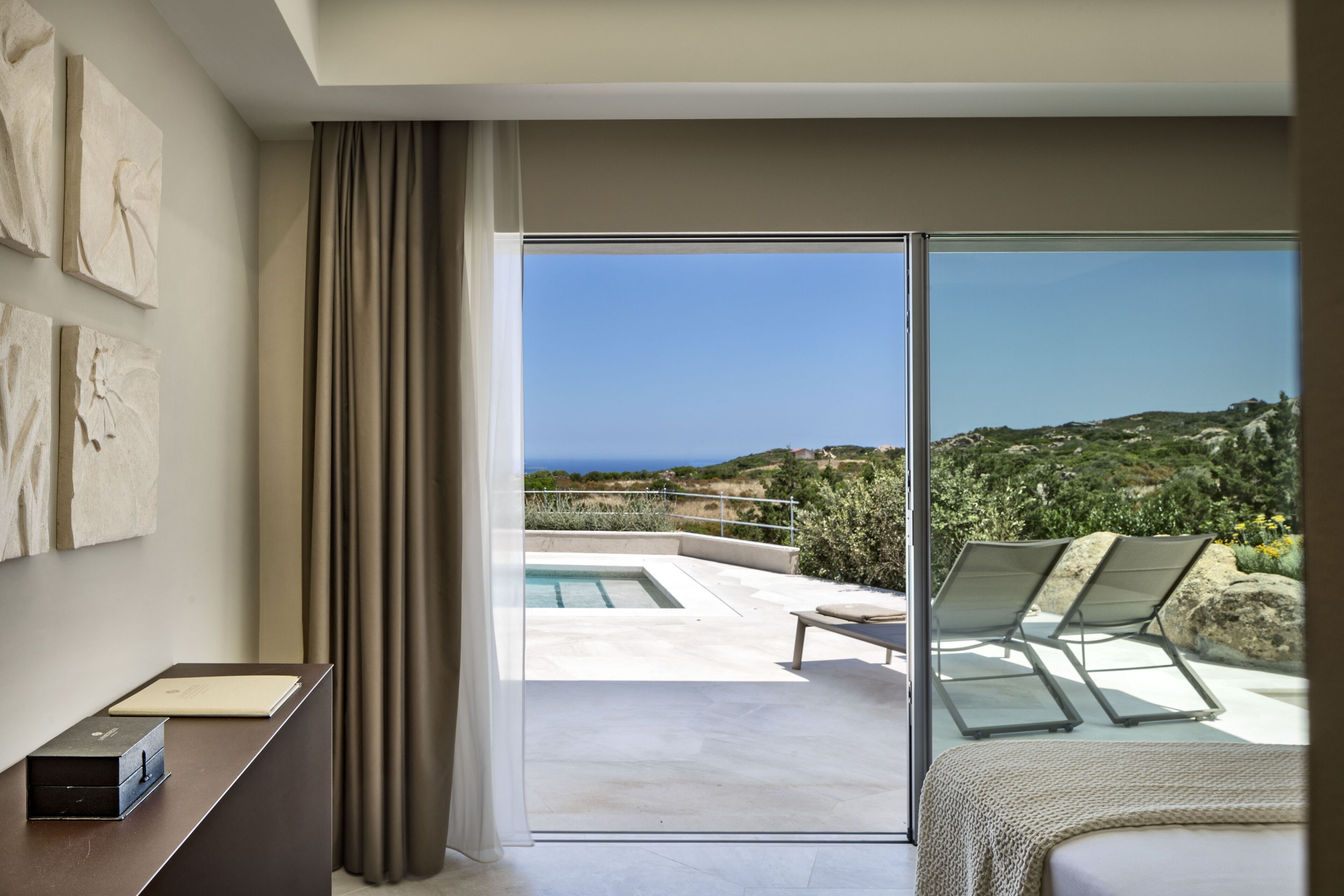 Una habitación de hotel moderna con un amplio ventanal corredero que da a una zona de piscina con vistas al océano.