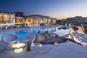 A poolside area with modern seating, a stone feature, and a view of the landscape. - Li Finistreddi Exclusive Country Retreat (Arzachena)