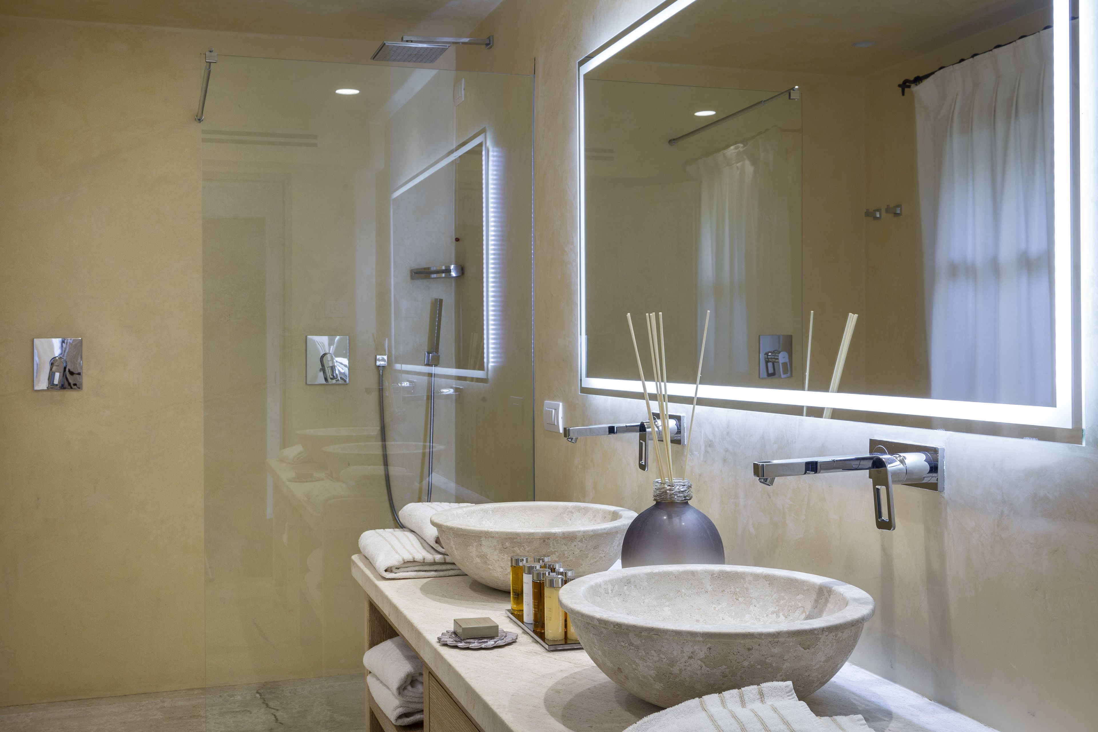 A modern bathroom with two large stone sinks, a large mirror, and a shower area.