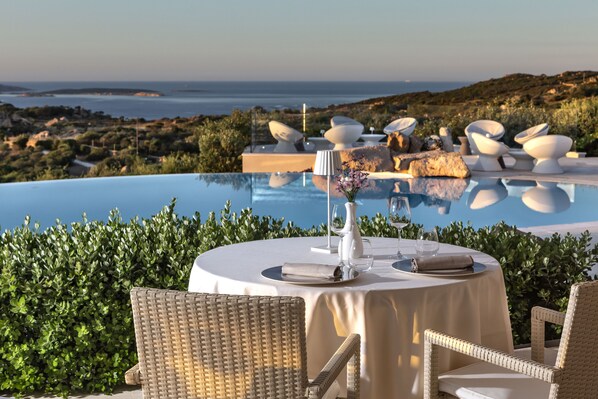 A dining area with a pool view, wicker chairs, and a table set for two. - Li Finistreddi Exclusive Country Retreat (Arzachena)