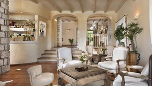 A spacious lobby with a bar area, multiple seating options including white leather chairs, a wooden coffee table, and a stone wall. - Li Finistreddi Exclusive Country Retreat (Arzachena)