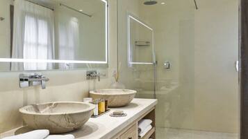 A modern bathroom with two marble sinks, a large mirror, and a glass-enclosed shower.