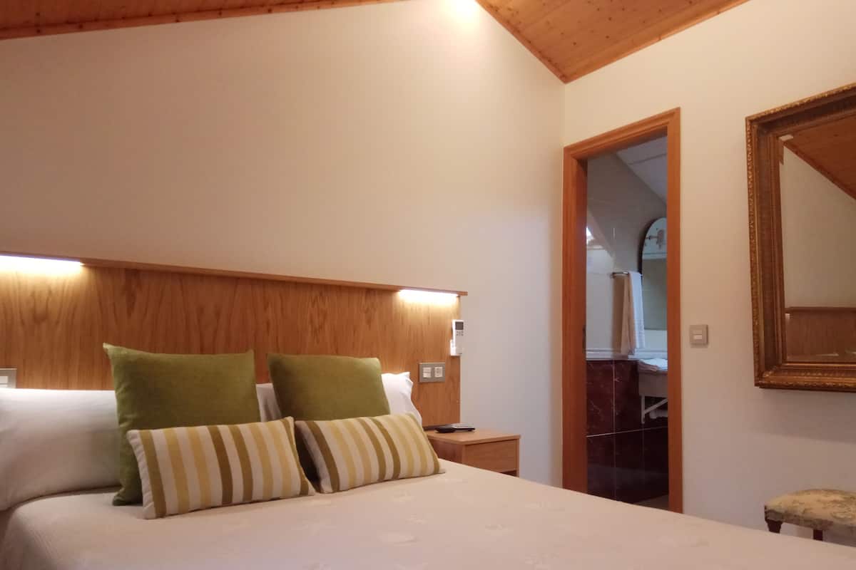 Une chambre d’hôtel avec un plafond en bois, un lit avec des oreillers verts et à rayures, une table de chevet avec une télécommande et un miroir sur le mur.