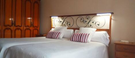 A neatly made bed with white linens and striped pillows, a wooden headboard with a decorative metal design, and a wooden nightstand with a lamp.