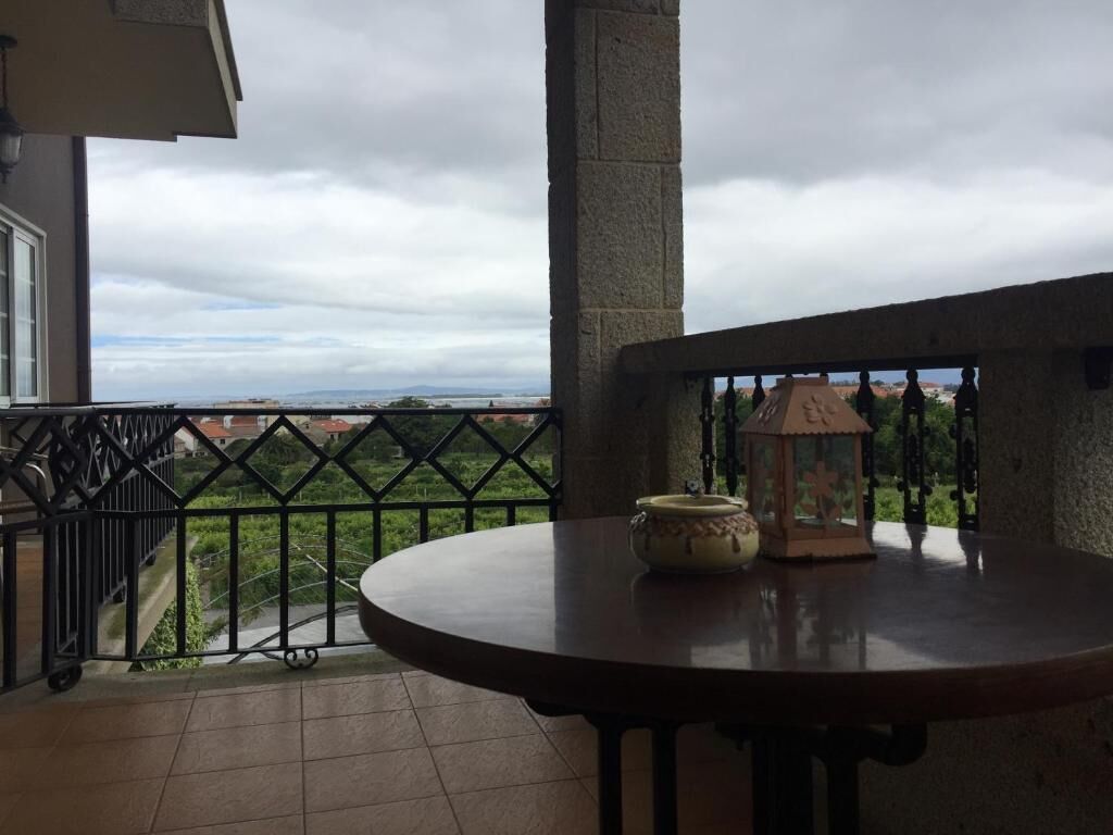 Een balkon met uitzicht op een veraf gelegen landschap, een ronde tafel met een vaas en een lantaarn, en een balustrade.