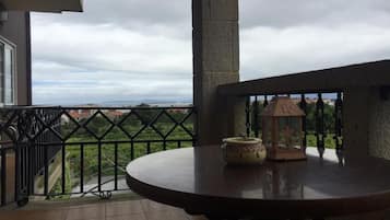 Een balkon met uitzicht op een veraf gelegen landschap, een ronde tafel met een vaas en een lantaarn, en een balustrade.