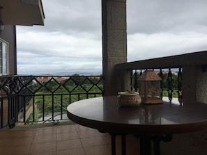 Un balcon donnant sur un paysage lointain, une table ronde avec un vase et une lanterne, et une balustrade.
