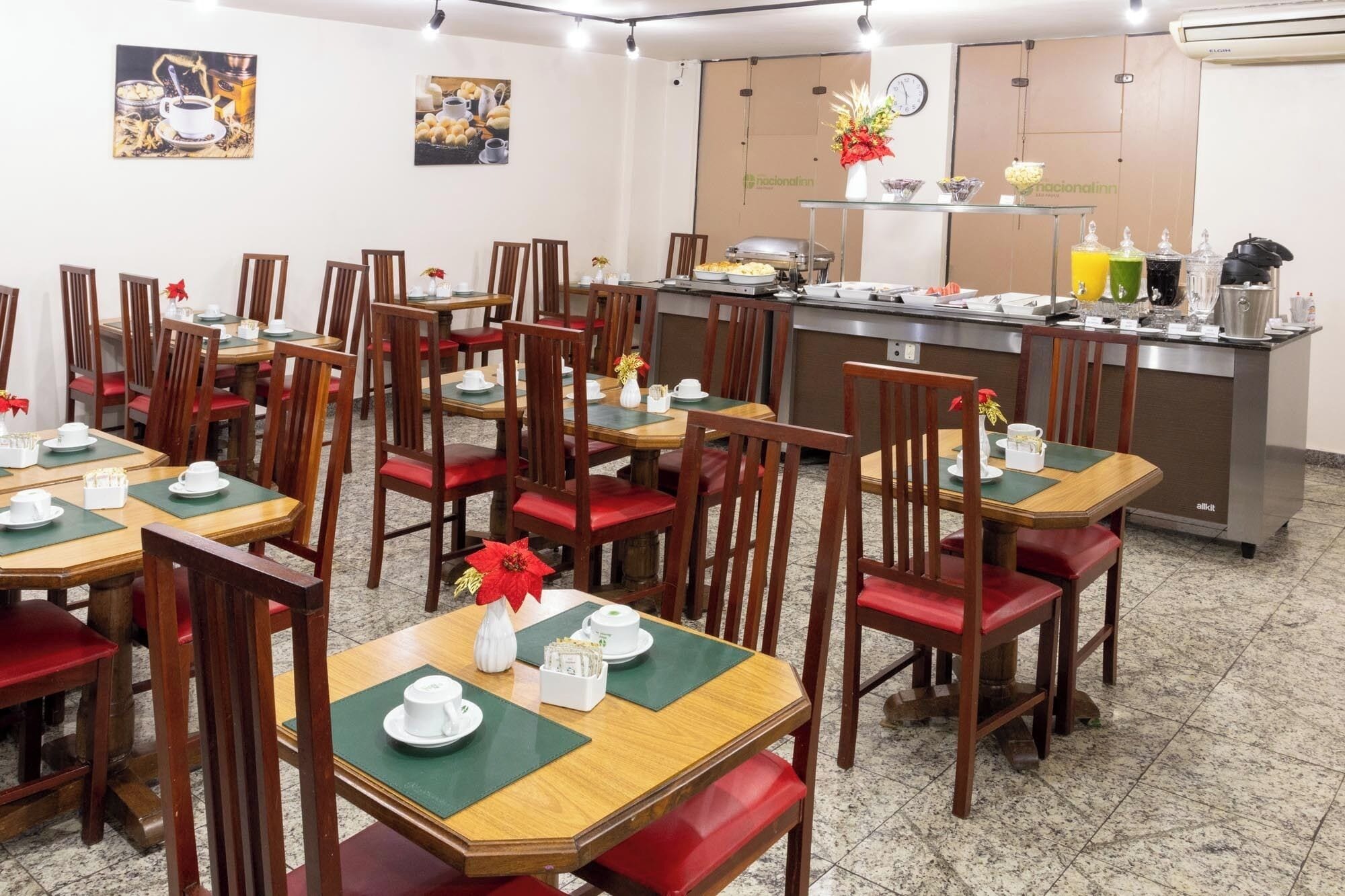 A restaurant with wooden tables and red cushioned chairs, a buffet counter, and wall art.