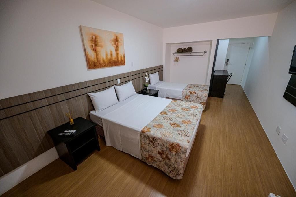 A hotel room with two beds, a small desk, a nightstand, a TV, and a painting on the wall.