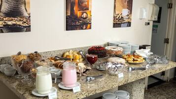 A buffet with various food items and beverages, including cakes, pastries, and dairy products, displayed on a granite counter.