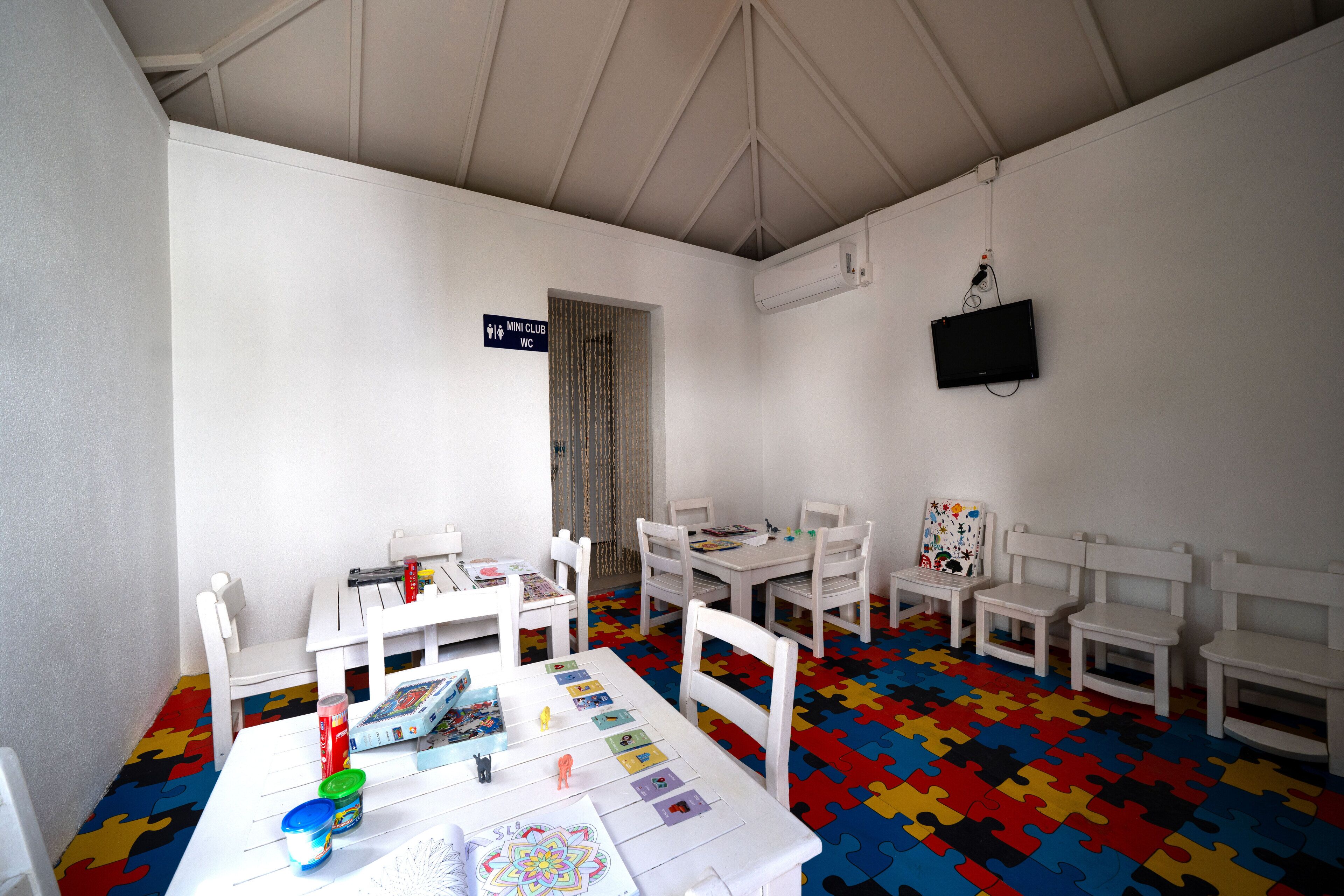 A children's playroom with white furniture, a colorful puzzle floor, and a TV mounted on the wall.