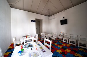 Una sala de juegos infantiles con mobiliario blanco, un suelo de puzzle de colores y un televisor montado en la pared.