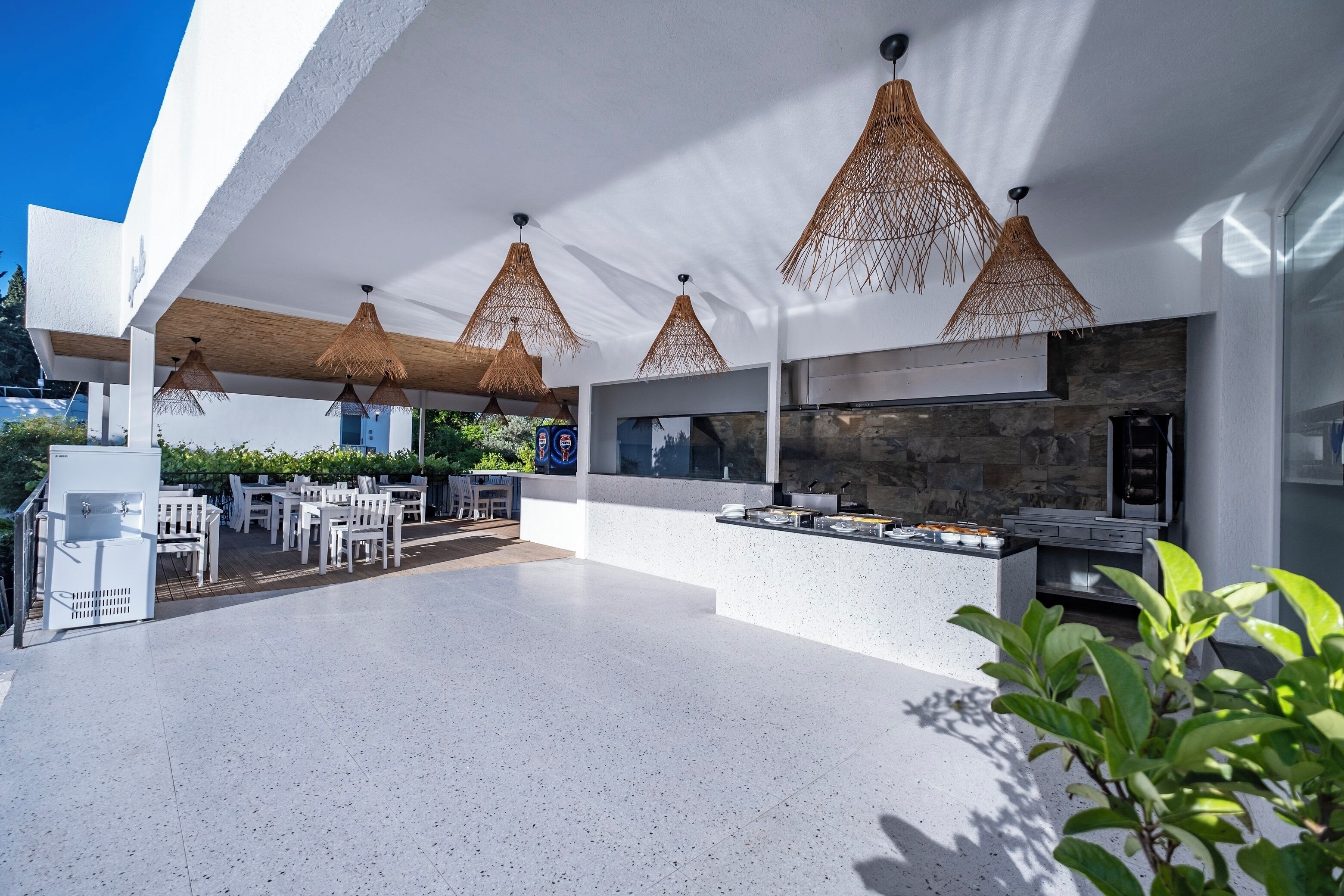 Una zona pranzo esterna moderna con mobili bianchi, un muro in pietra e lampade in rattan sospese.