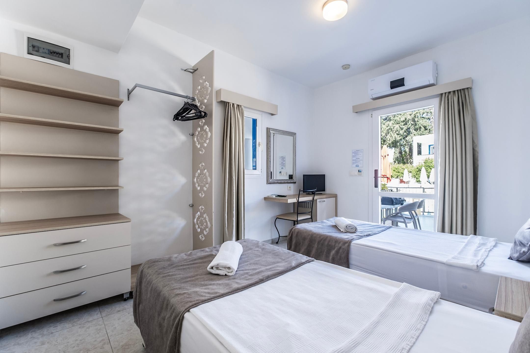 A hotel room with two beds, a desk with a computer, a chair, and a wardrobe.