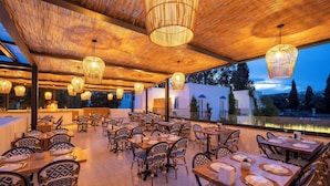 An outdoor dining area with wicker chairs and tables, overhead wicker chandeliers, and a view of the landscape. - Paloma Family Club  (Bodrum)
