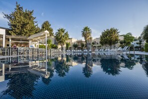 A swimming pool with lounge chairs and a covered seating area, surrounded by palm trees and buildings.