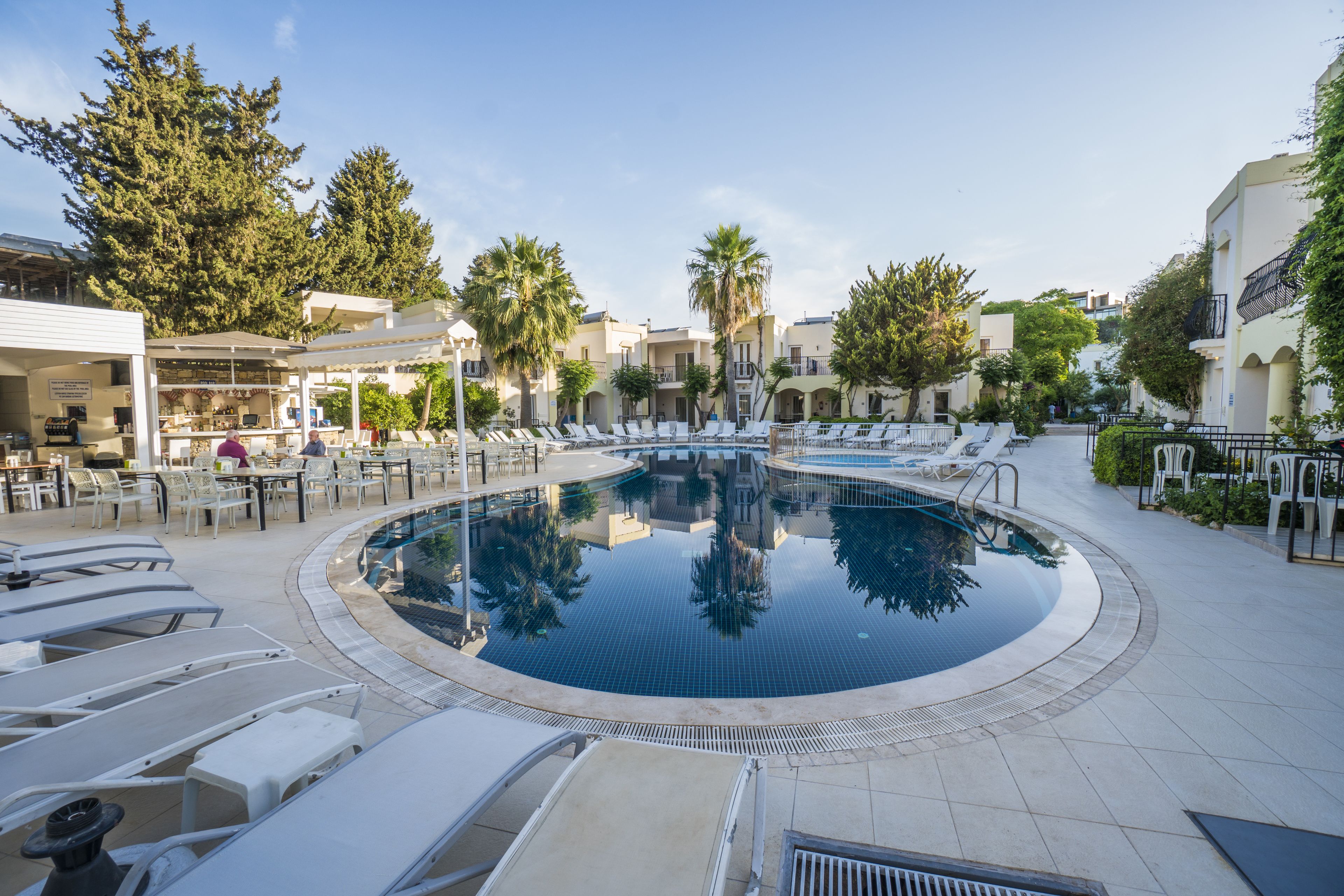 A pool area with lounge chairs, a bar, and a building with a terrace.