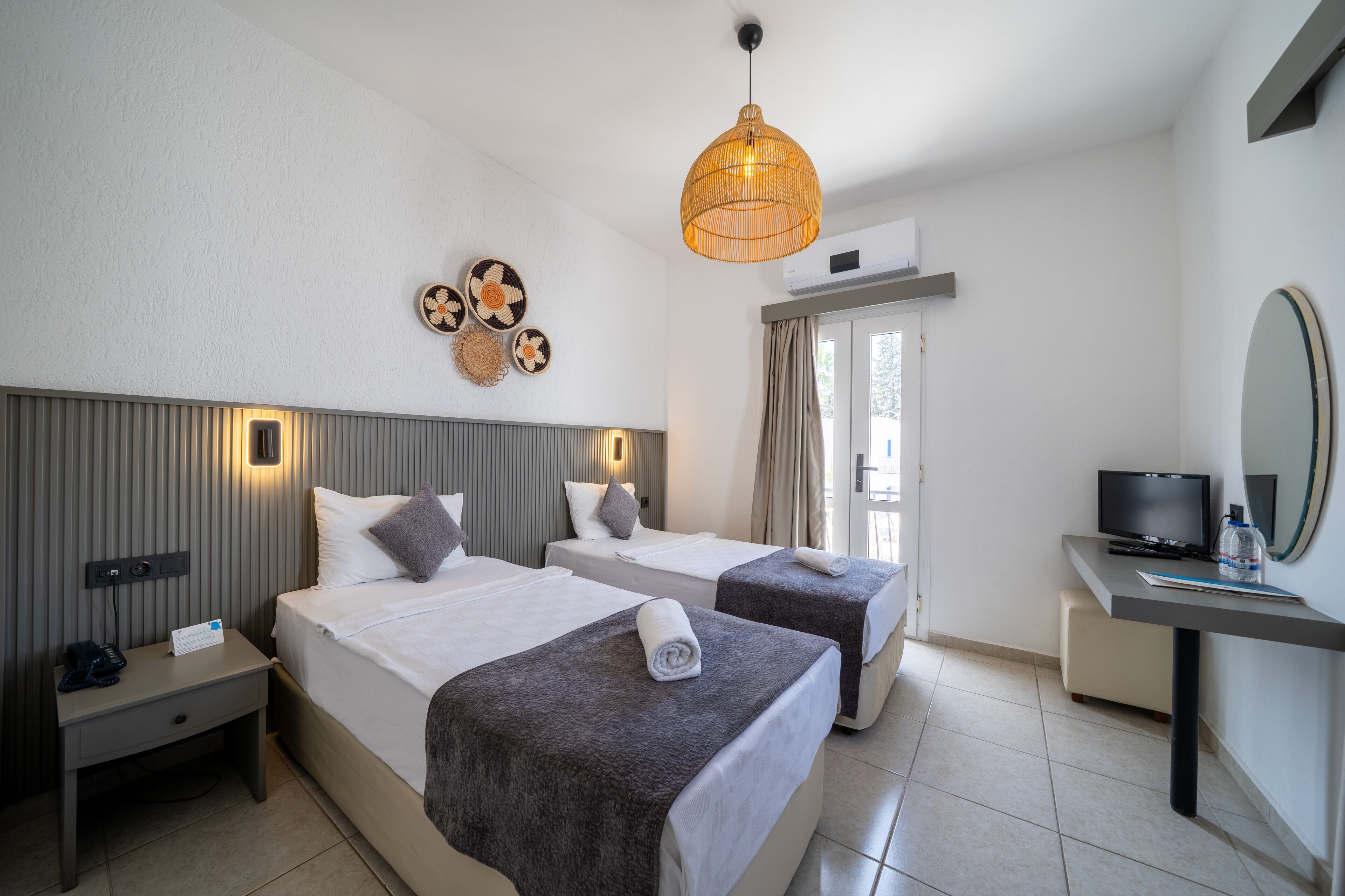 Habitación de hotel con dos camas, un escritorio, un televisor y un ventanal grande.