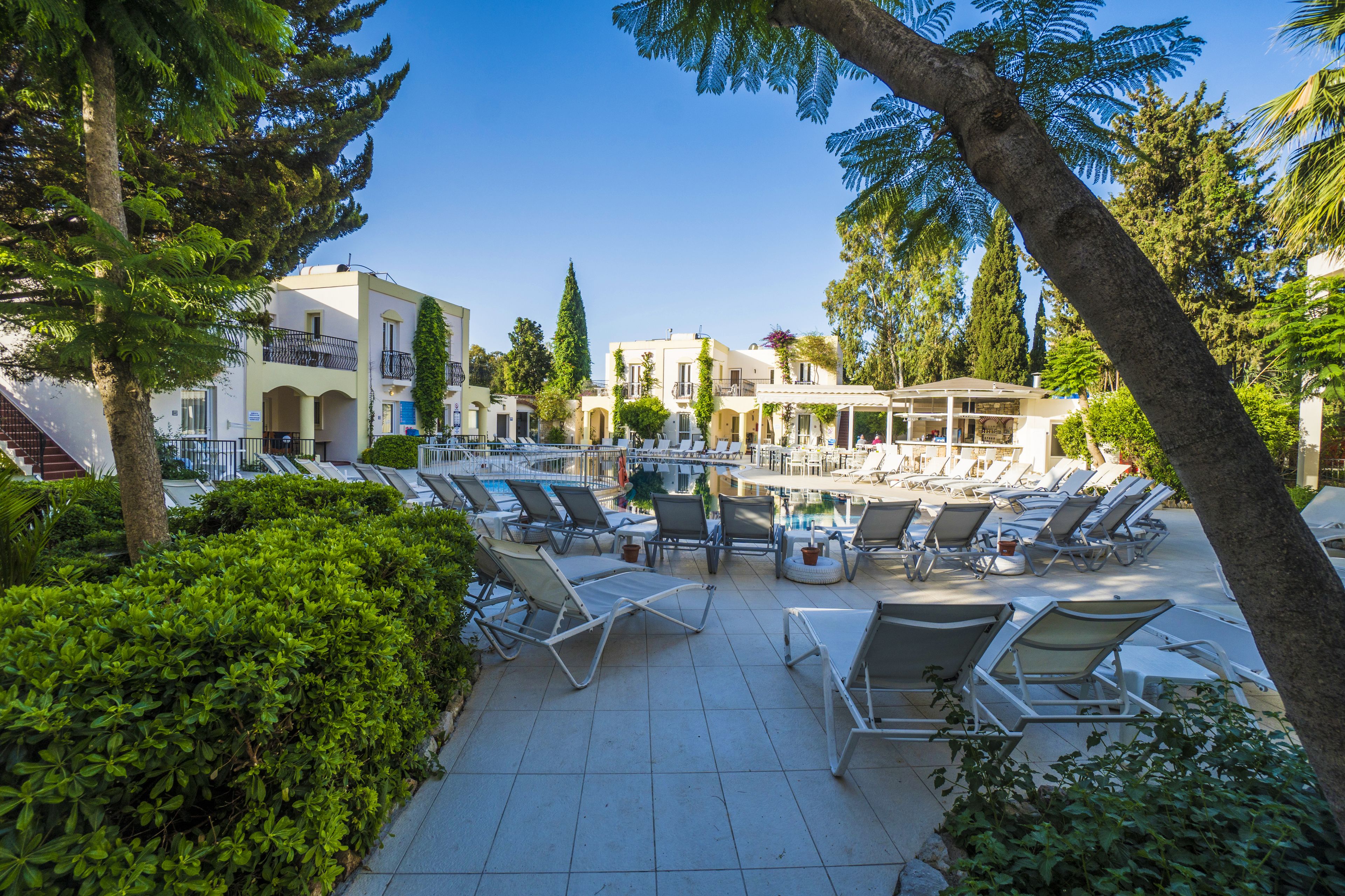 Un espace aménagé au bord de la piscine, avec des chaises longues, un coin salon couvert et un bâtiment doté de balcons.