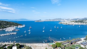A marina with numerous boats docked, a beach area with umbrellas, and a coastal town in the background. - Paloma Family Club  (Bodrum)
