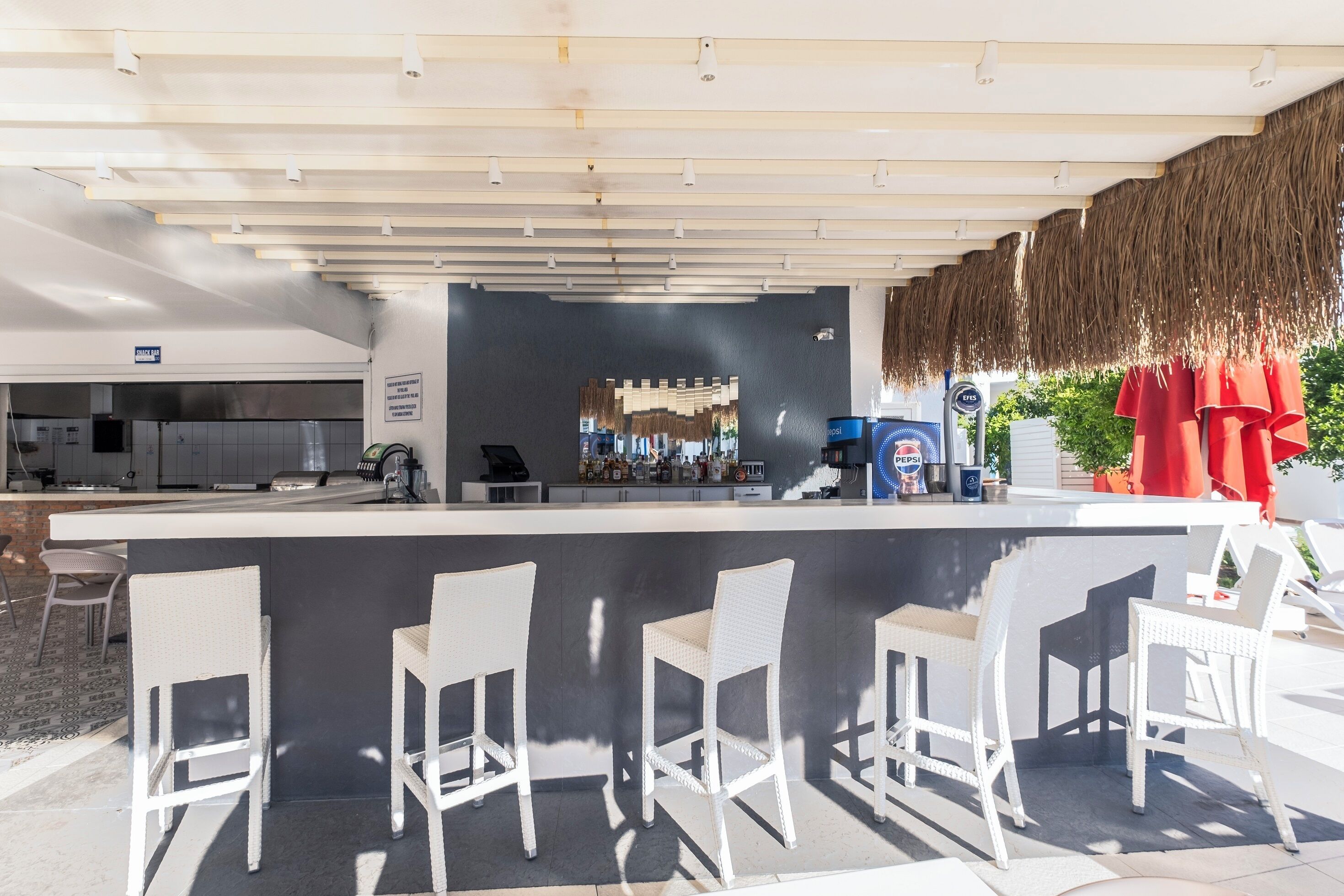Ein Außenbereich mit Bar, einer Theke, weißen Stühlen und einer Küche im Hintergrund.