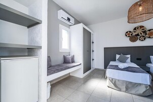 A modern bedroom with a built-in bench, a bed with a grey headboard, and a wall-mounted air conditioner.