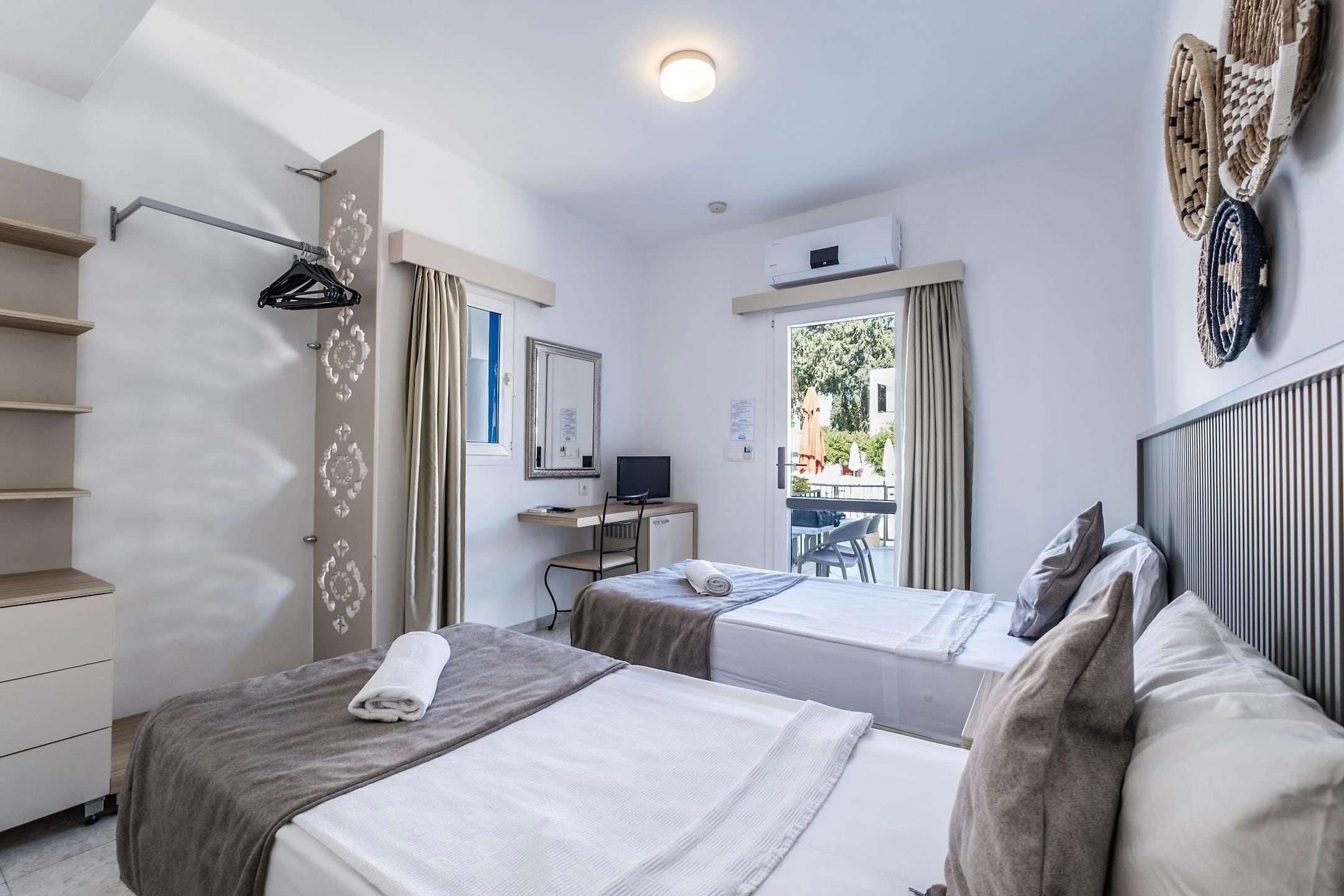 A hotel room with two beds, a desk with a computer, a chair, and a view of the outdoors.