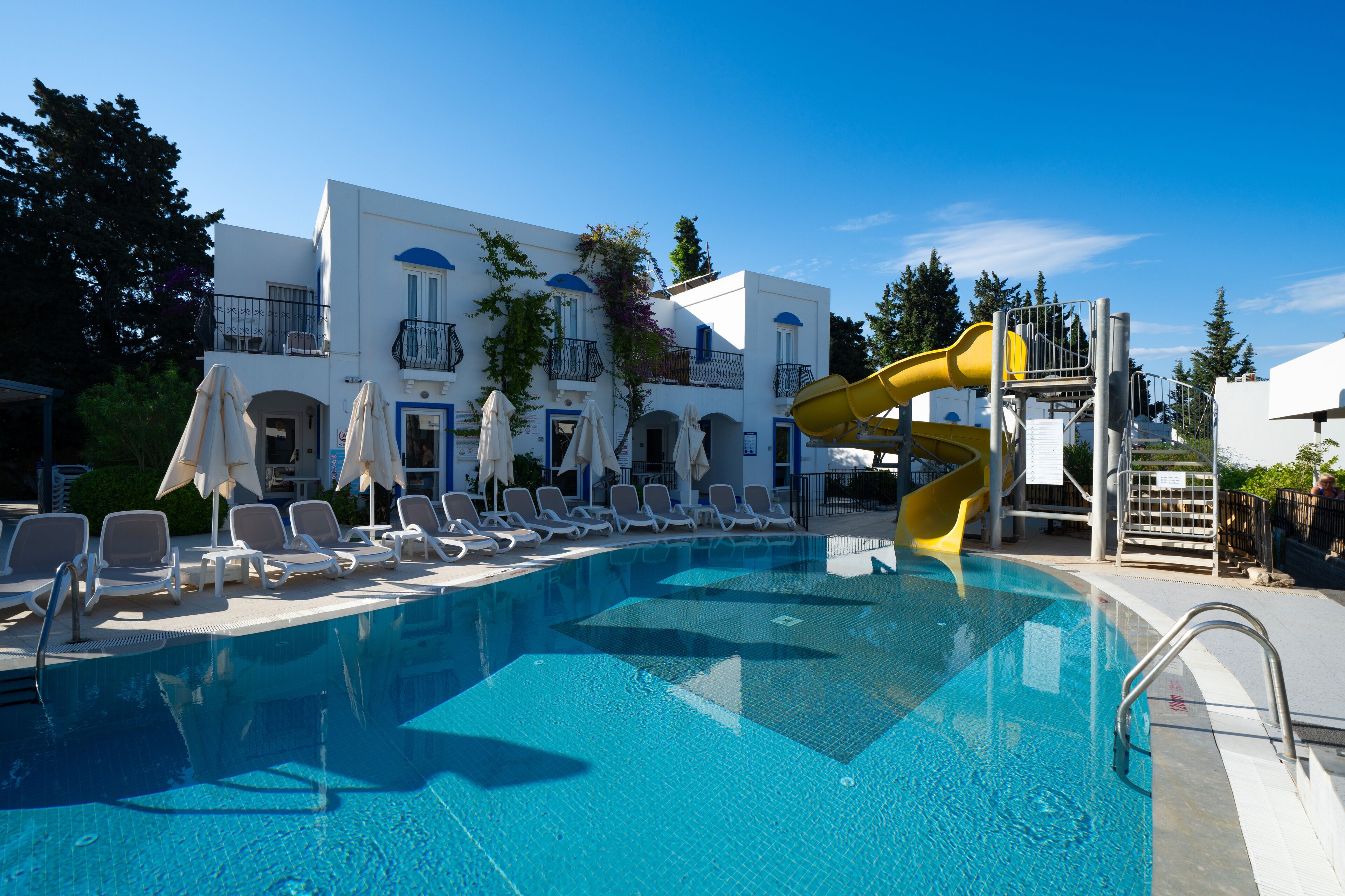 A swimming pool with lounge chairs and a yellow slide.