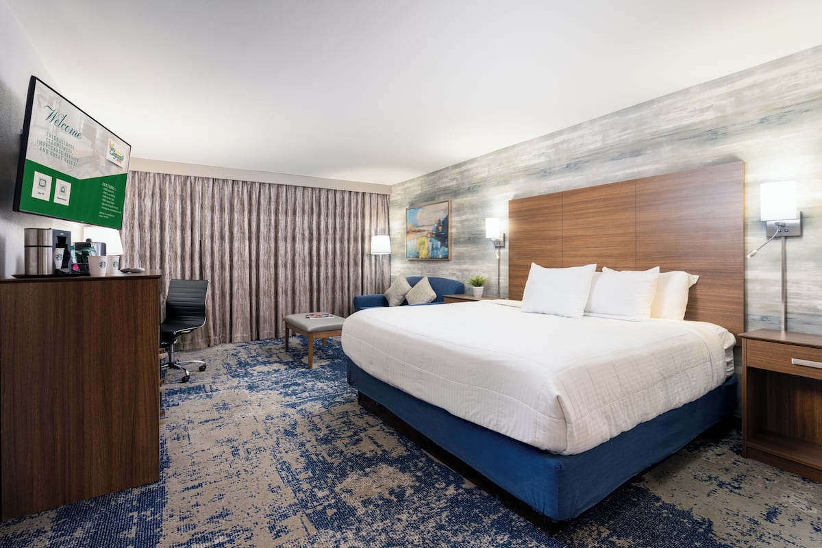 Habitación de hotel con una cama grande, un escritorio, una silla, una mesita y un televisor mostrando un mensaje de bienvenida.