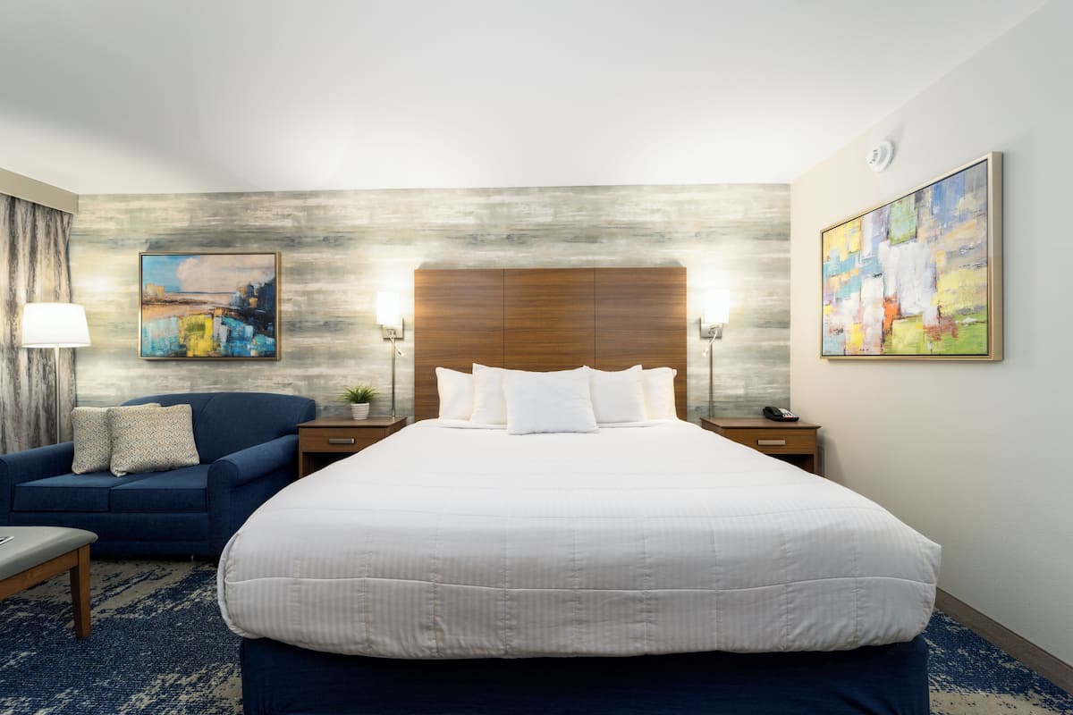 Habitación de hotel con una cama grande, un sofá azul, una lámpara y dos cuadros en las paredes.