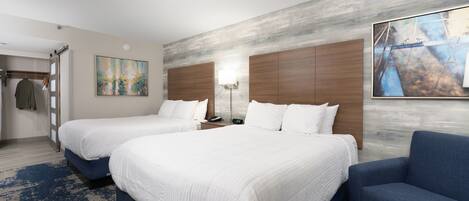 Habitación de hotel con dos camas, un sillón azul, un cuadro en la pared y un cabecero de madera.