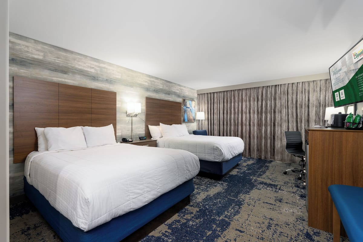 Habitación de hotel con dos camas, un escritorio, una silla y un cuadro grande en la pared.