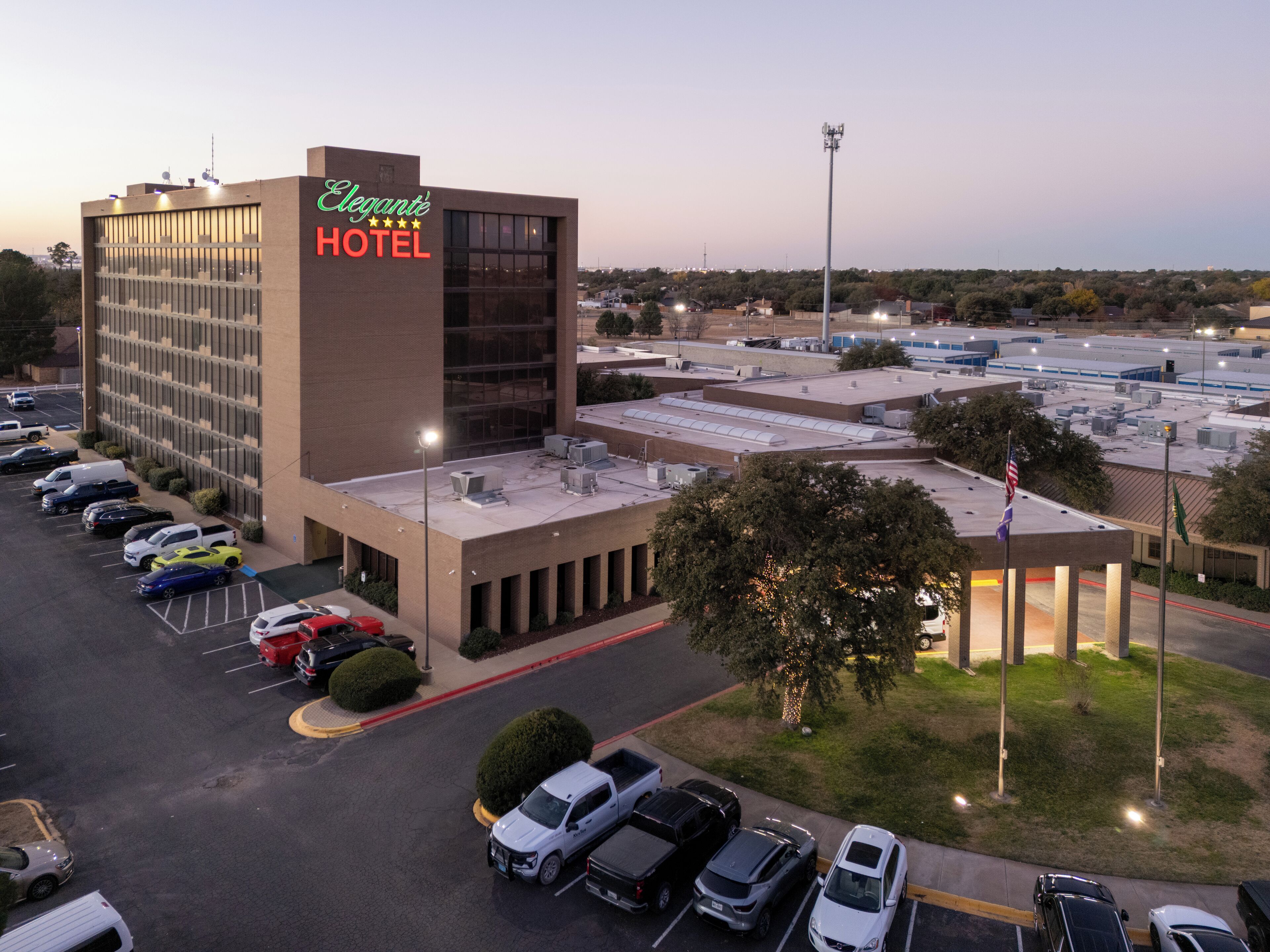 A hotel with a large parking lot, a building with a sign reading "Elegant Hotel", and a flagpole with flags.