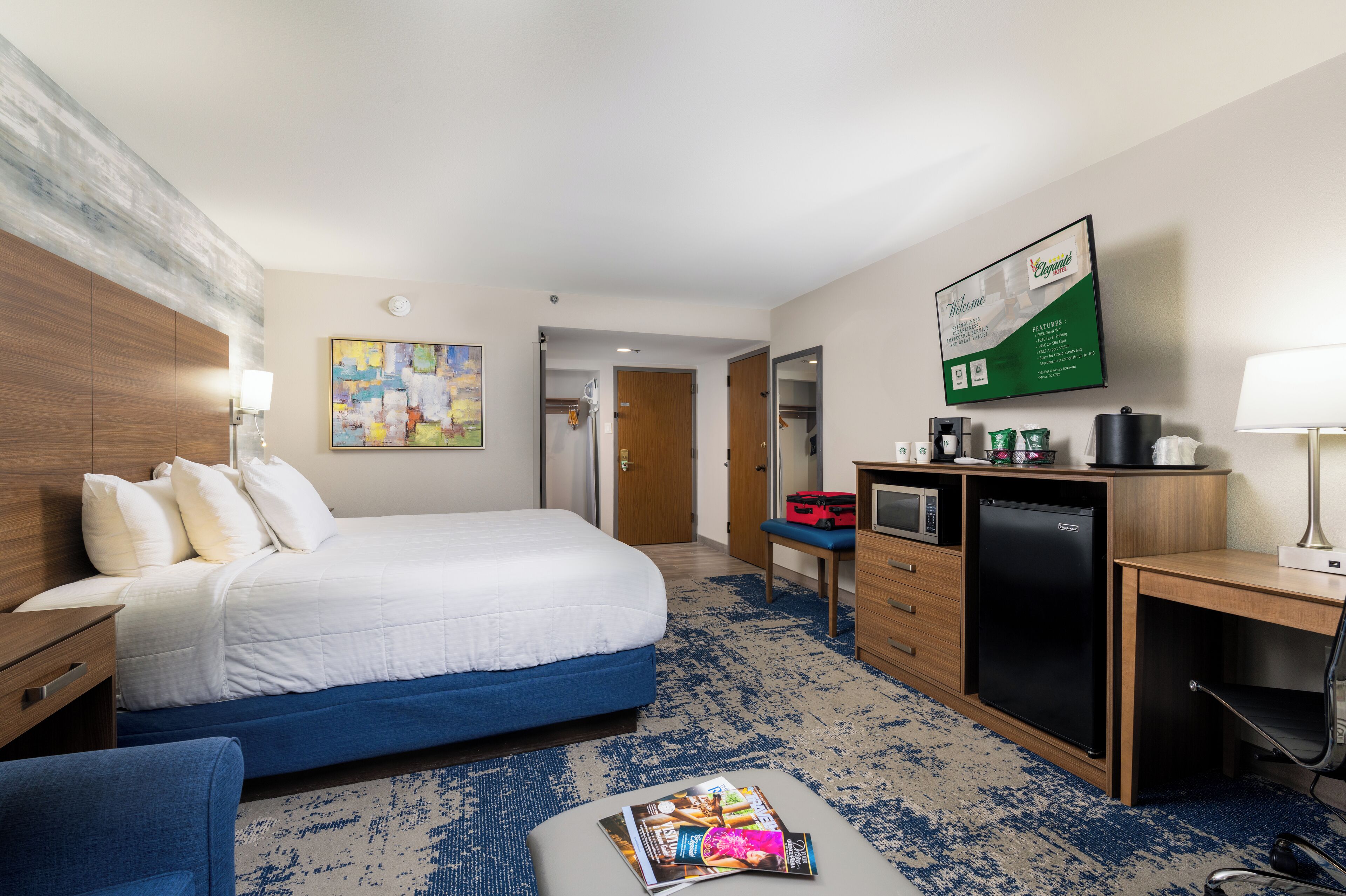 Een hotelkamer met een bed, bureau, kitchenette en een schilderij aan de muur.