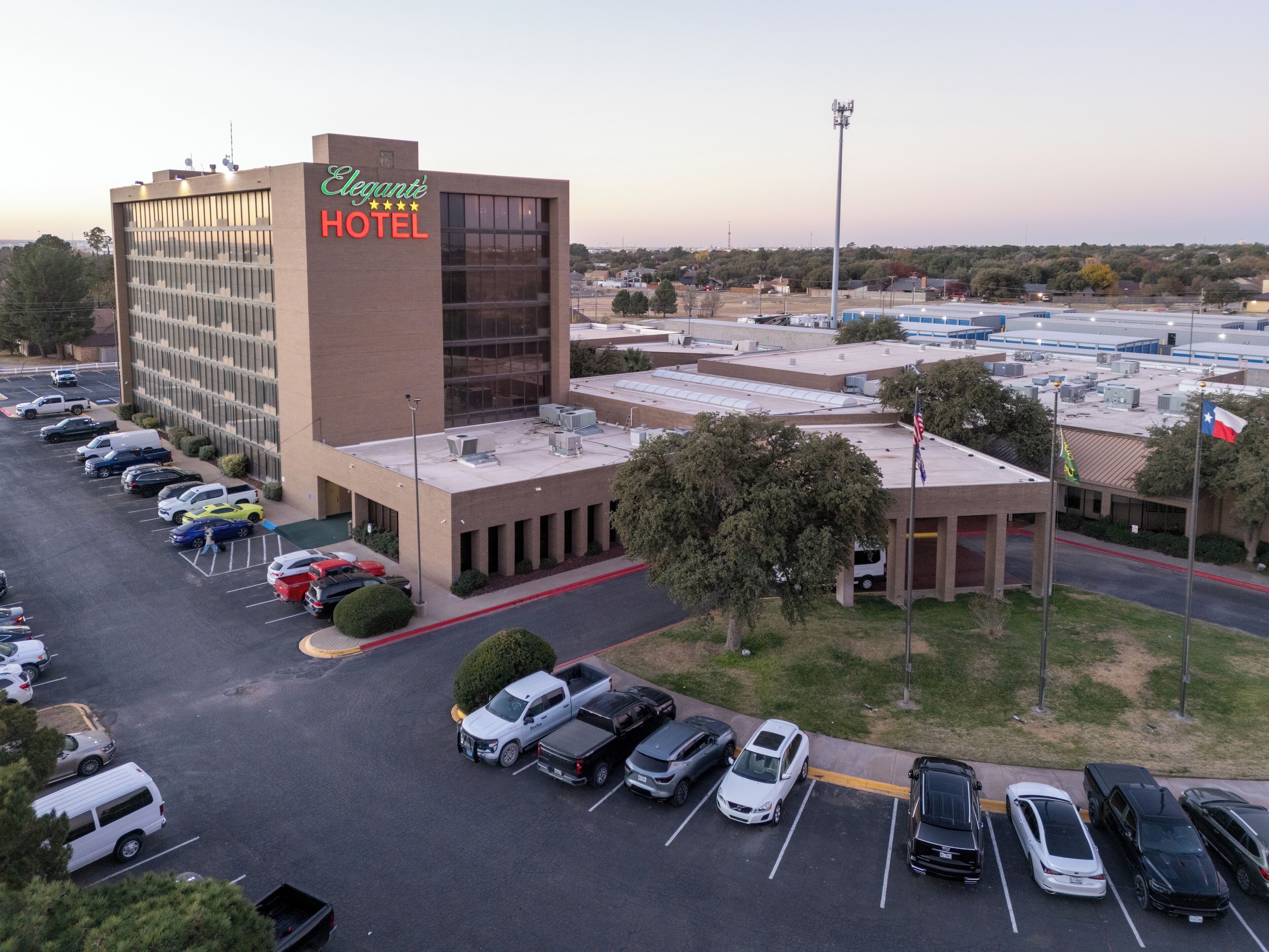 An aerial view of the Elegant Hotel with a parking lot, a large building, and surrounding landscape.