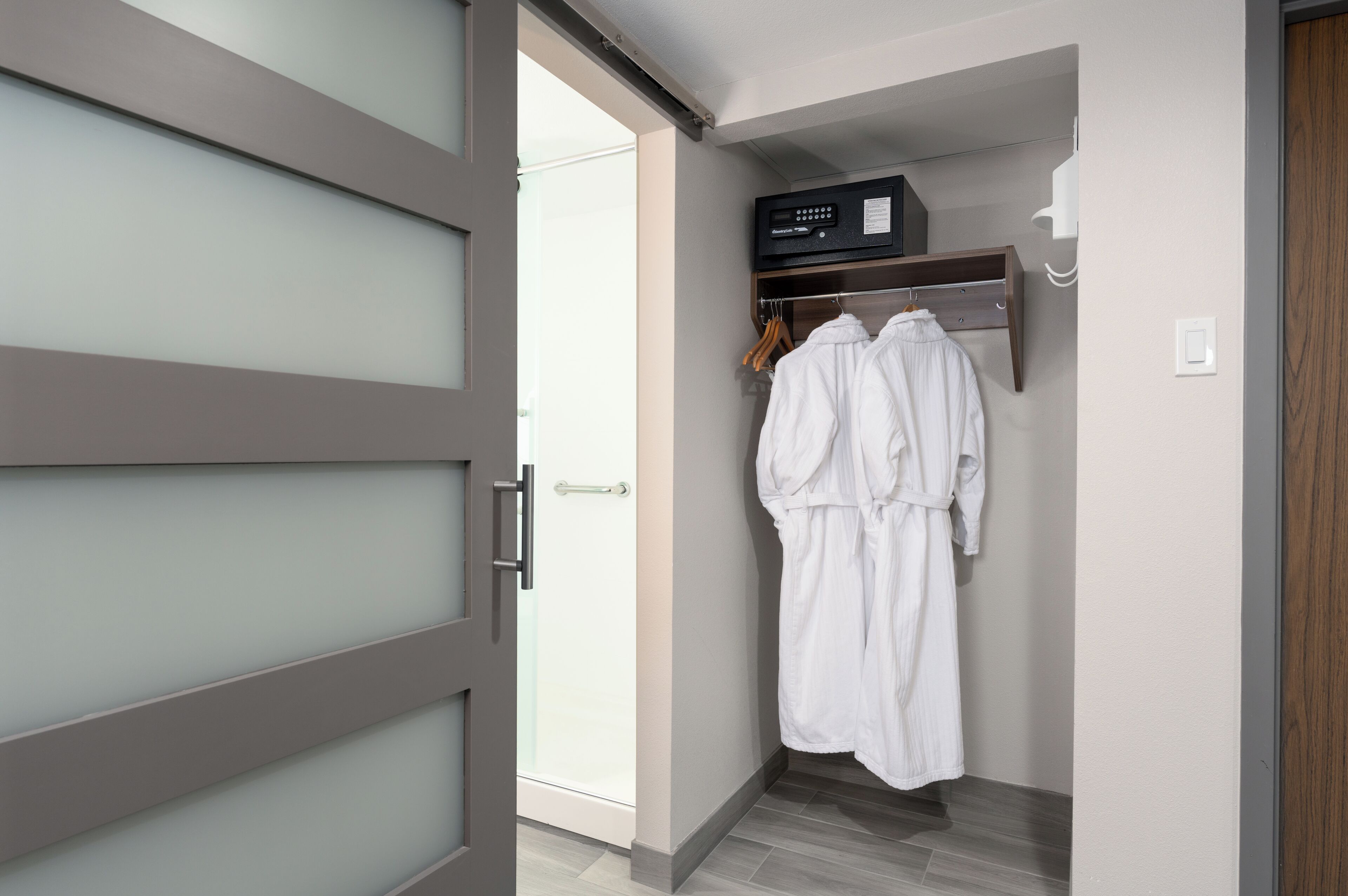 A modern bathroom with a glass shower door, a wooden vanity, and a robe hanging on a rack.