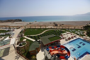 A resort with a swimming pool, water slide, and beach view.