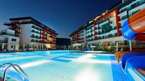A swimming pool with a slide, surrounded by modern buildings with balconies and outdoor seating. - Ulu Resort Hotel - All Inclusive (Gülnar)
