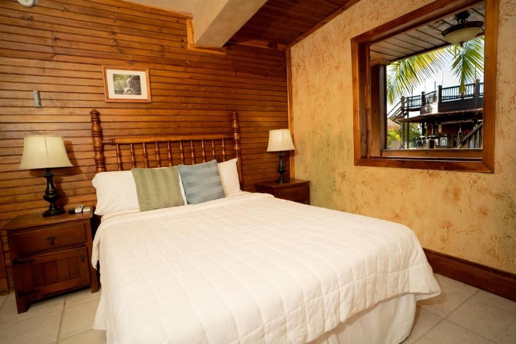 A bedroom with a wooden headboard, two bedside tables with lamps, a bed with a white quilt, and a window with a view of a balcony.
