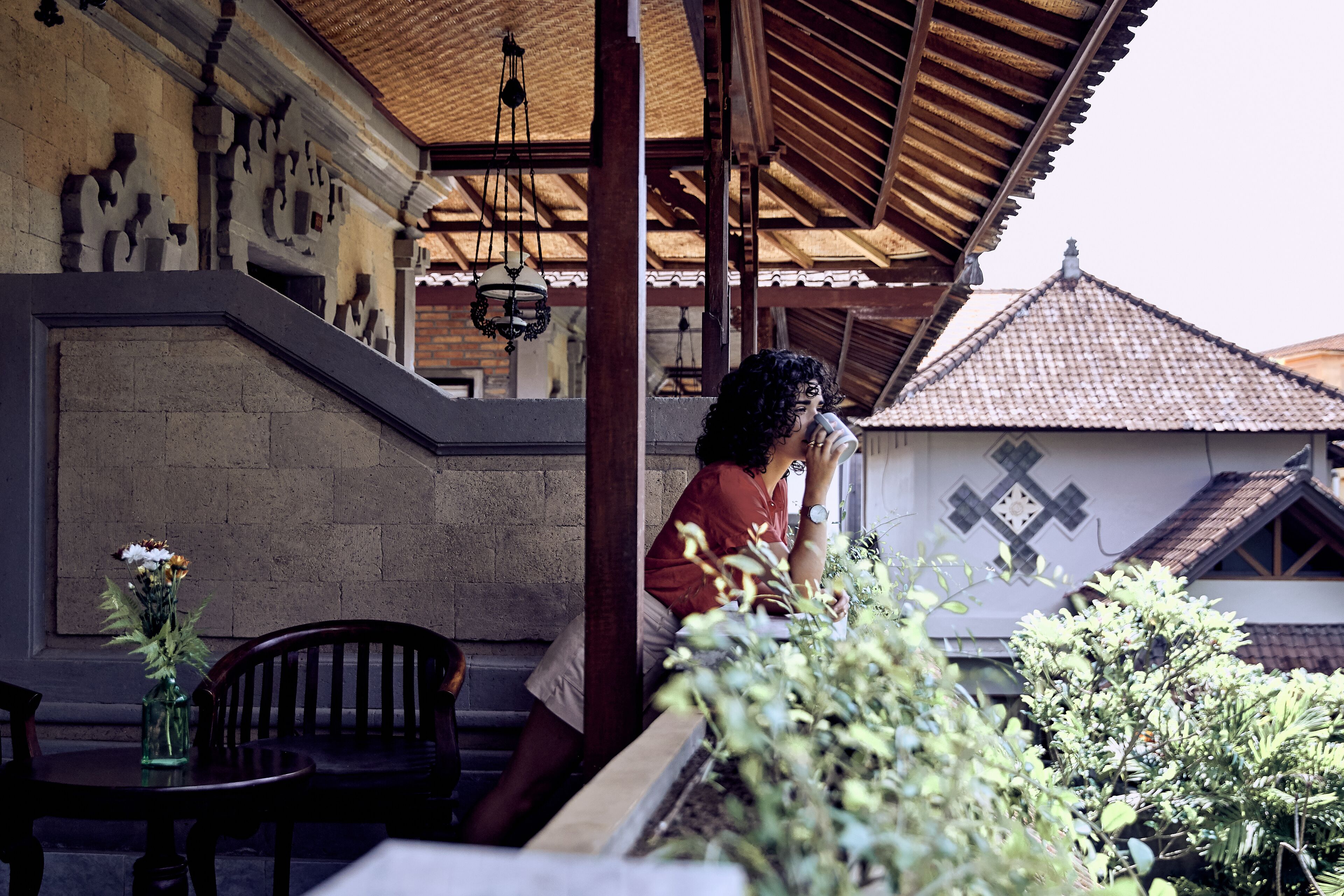 A covered outdoor seating area with a stone wall and a tiled roof in the background.