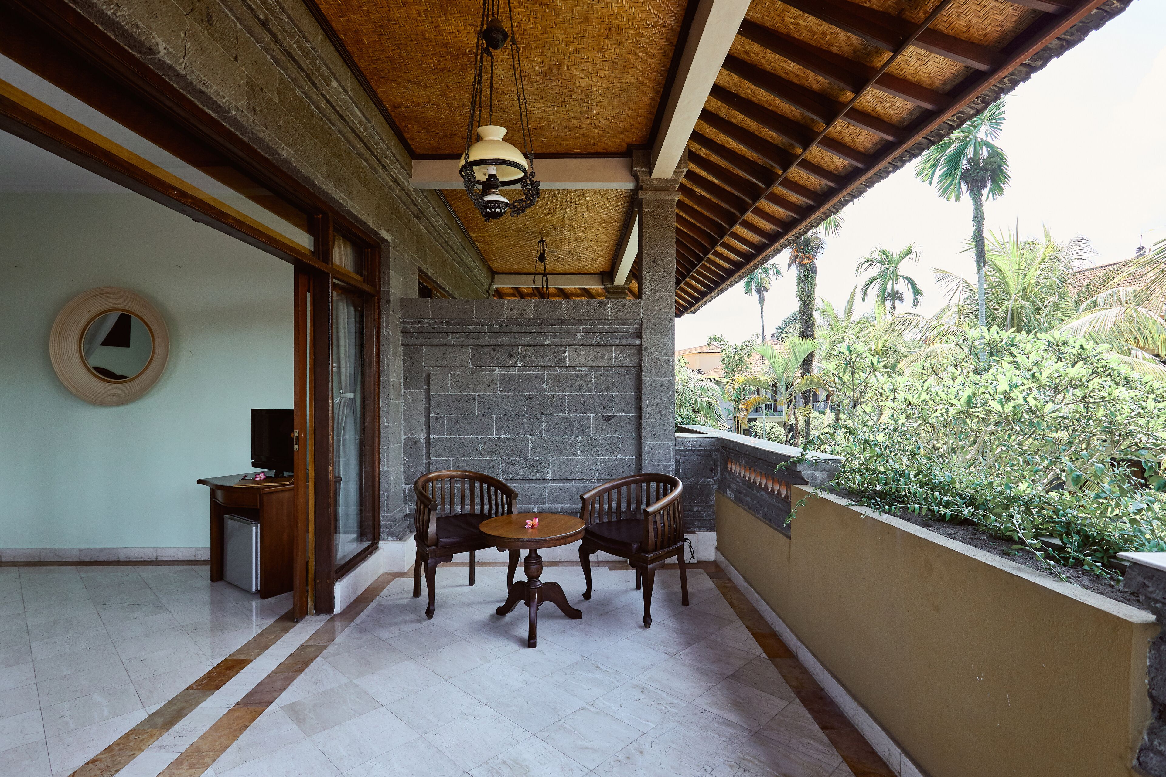 A covered patio with a table and chairs, a hanging light fixture, and a view of greenery outside.