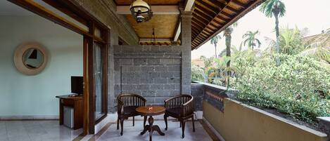 A covered patio with a table and chairs, a hanging light fixture, and a view of greenery outside.