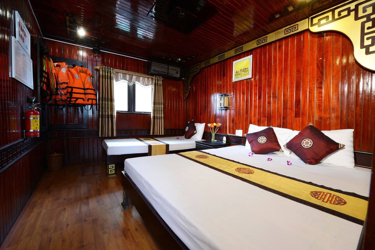 Quarto de hotel com duas camas, paredes de madeira, um extintor de incêndio e uma janela com cortinas.