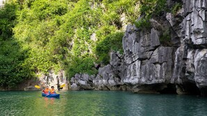 A kayak on a calm river with rocky cliffs and dense greenery in the background. - Imperial Legend Cruise Halong (Tuan Chau)