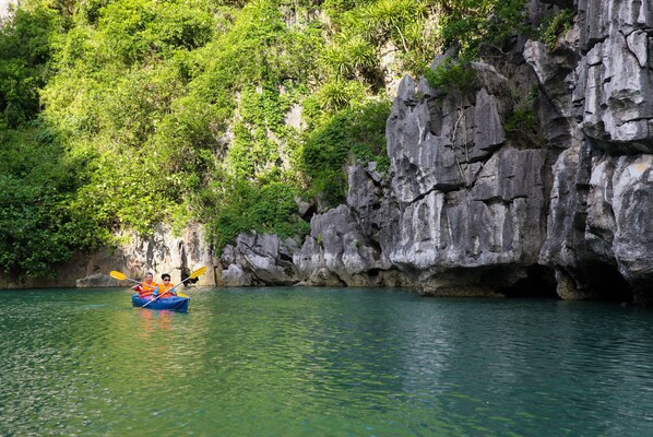A kayak on a calm river with rocky cliffs and dense greenery in the background. - Imperial Legend Cruise Halong (Tuan Chau)