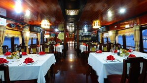 A restaurant with tables set for dining, a bar in the background, and a view of the sea through large windows. - Imperial Legend Cruise Halong (Tuan Chau)