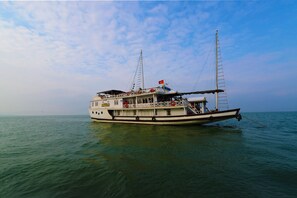 A large boat with a cabin and deck area, floating on calm water. - Imperial Legend Cruise Halong (Tuan Chau)