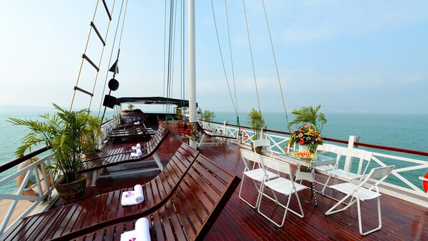 A wooden deck with lounge chairs, a table with fruit, and potted plants. - Imperial Legend Cruise Halong (Tuan Chau)